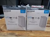 deux boîtes contenant des routeurs Wi-Fi Netgear Orb posées sur une table en bois