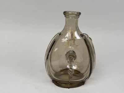 un vase en verre muni d'une poignée en argent, posé sur un fond blanc