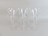 six verres à vin transparents sont alignés sur une surface blanche