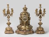 trois bougeoirs dorés et une horloge posés sur une table