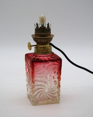 une image représentant un flacon de parfum en verre rouge et blanc surmonté d'une lampe
