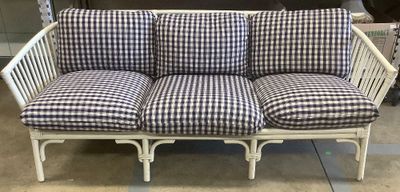 une causeuse en osier blanc avec des coussins à carreaux bleus et blancs