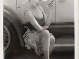 black and white photograph of a woman sitting on a car holding a cigarette