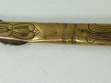 a gold colored knife with a black handle on a white surface