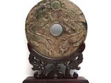 a carved stone disk on a stand on a white background
