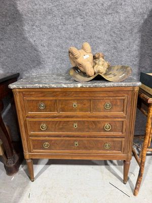 une commode au plateau en marbre, sur laquelle est posé un chapeau
