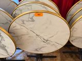 six round marble tables with gold rims on stands in front of a red curtain