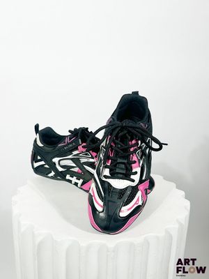 une paire de chaussures de course noires et roses posées sur un socle blanc