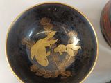 a black bowl with gold designs on it next to a black vase