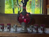 un vase rouge et des tasses posés sur une étagère en bois