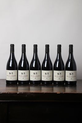 six bouteilles de vin sont posées sur une table devant un mur blanc