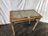 an old wooden table with a glass top and wooden legs
