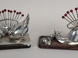 deux sculptures métalliques représentant des escargots, ornées de perles rouges, posées sur un socle en bois