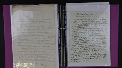 un livre ouvert, sur lequel repose une lettre manuscrite, posé sur une table