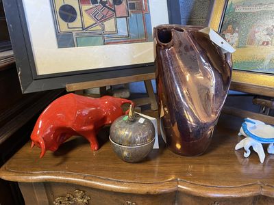 un vase marron posé sur une table, avec un cochon rouge et un cochon bleu