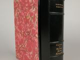 an old black book with a pink cover sitting on top of a white table