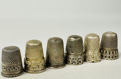 six antique thimbles lined up in a row on a white surface