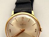 une montre en or avec un bracelet noir sur un fond blanc