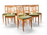 quatre chaises en bois avec des assises rembourrées vertes, posées sur une surface blanche