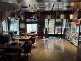 Des tables et des chaises sont alignées dans un restaurant, avec un réfrigérateur en arrière-plan.