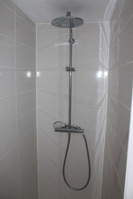 a shower head in the corner of a white tiled bathroom