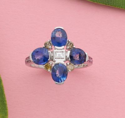 un gros plan d'une bague sertie d'un saphir bleu et de diamants, posée sur un fond rose