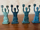 quatre figurines représentant des femmes levant les mains, posées sur une table en bois