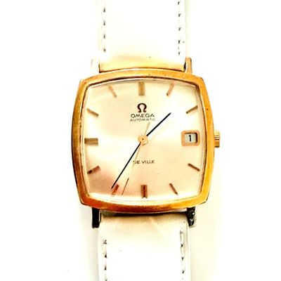 une montre en or avec un bracelet en cuir blanc posée sur une surface blanche