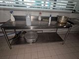 une table en acier inoxydable sur laquelle sont posés des casseroles et des poêles, dans une cuisine