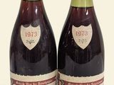 two bottles of red wine sitting next to each other on a white surface