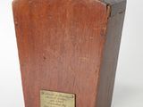 une vieille boîte en bois ornée d'une plaque, posée sur une surface blanche
