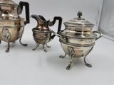 two silver teapots and a coffee pot sitting on a table