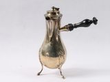 une cafetière ancienne en métal argenté, avec une poignée noire sur fond blanc