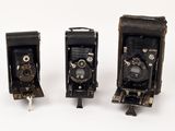 three old cameras sitting side by side on a white surface