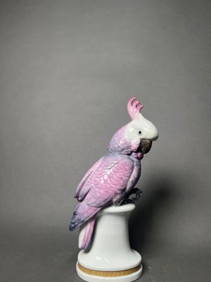 a figurine of a pink cockatoo sitting on top of a white vase