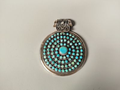 un gros plan d'un pendentif en argent et turquoise sur une surface blanche