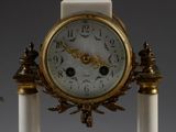 a white and gold clock sitting on top of a marble pedestal