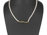 un collier de perles blanches muni d'un fermoir en or, posé sur un mannequin