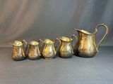 five antique silverplated jugs and a pitcher on a grey background