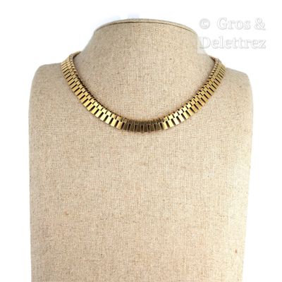 Le collier est en métal doré et comporte une chaîne qui y est fixée.