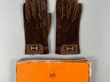 une paire de gants en cuir marron posée sur une boîte orange