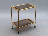 brass bar cart with glass shelves on casteors on a gray background