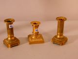 trois bougeoirs dorés posés sur une surface blanche
