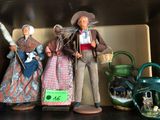 trois figurines représentant des personnes, posées côte à côte sur une étagère