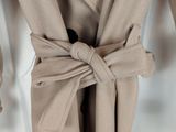 Le manteau est de couleur beige et comporte un grand nœud sur le devant.