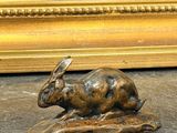 une sculpture en bronze représentant un lapin assis sur un rocher