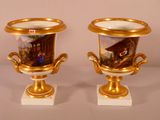 two gold vases with paintings on them sitting on a table
