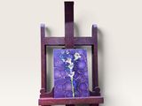 tableau posé sur un chevalet en bois, représentant des fleurs violettes et bleues