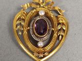un gros plan d'une broche en or ornée d'une pierre violette entourée de perles