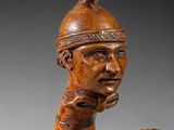wooden statue of a man with a helmet on his head holding a vase